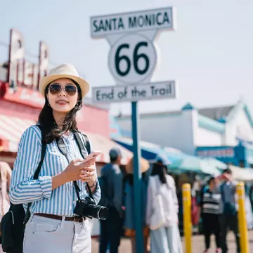 A woman stands on the pier in Santa Monica near a large sign marking the end of Route 66