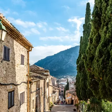 A sloping cobbled street of old stone houses leading down toward a mountain in a Mediterranean village.