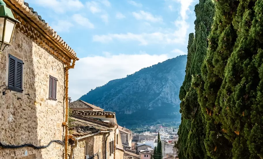 A sloping cobbled street of old stone houses leading down toward a mountain in a Mediterranean village.