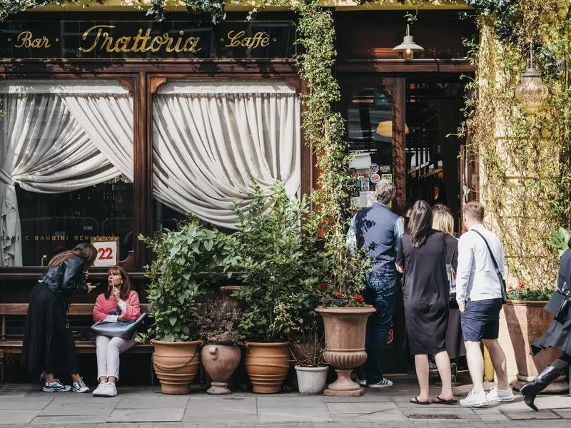 People by the front entrance of Gloria, Italian restaurant in Shoreditch, London, famous for ivy-covered exterior walls and numerous plants in terracotta pots outside.