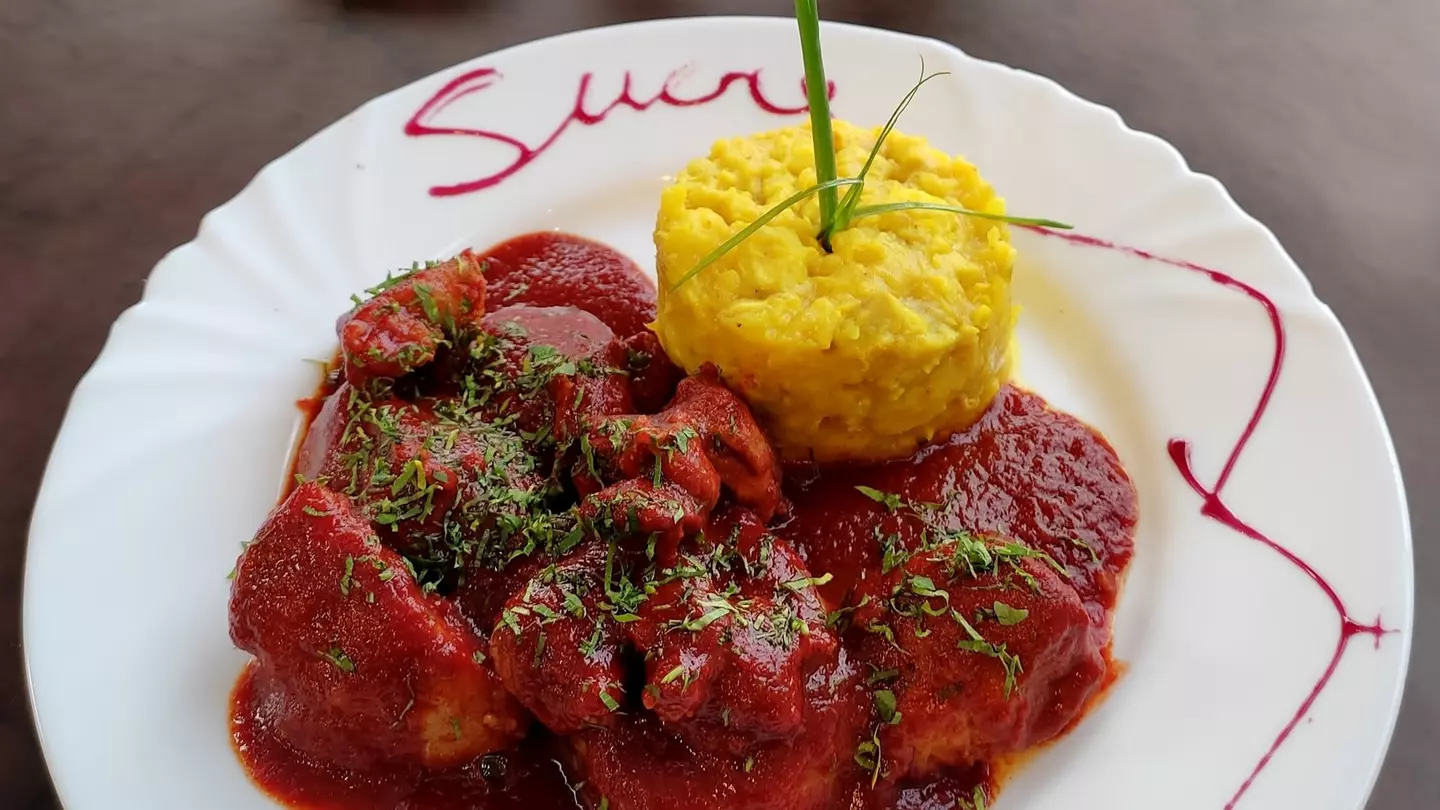 Bolivian pork dish Mondongo. The meat is stewed in a sweet paprika sauce served alongside two starches, potatoes and corn