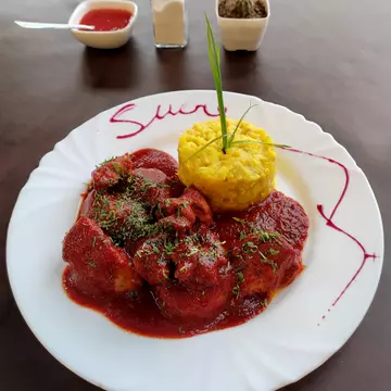 Bolivian pork dish Mondongo. The meat is stewed in a sweet paprika sauce served alongside two starches, potatoes and corn