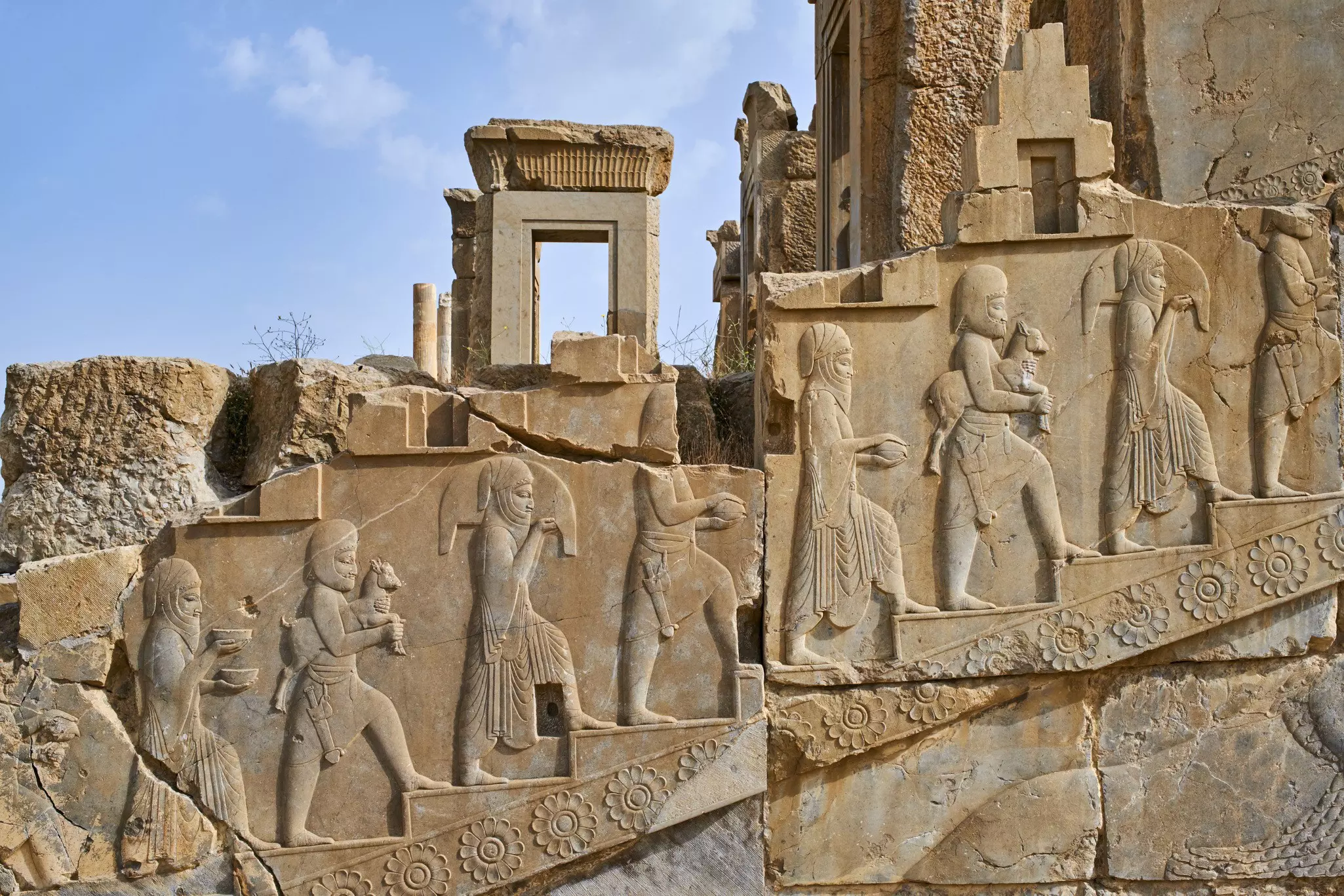 Relief carvings on an ancient ruined wall showing figures going up stairs.
