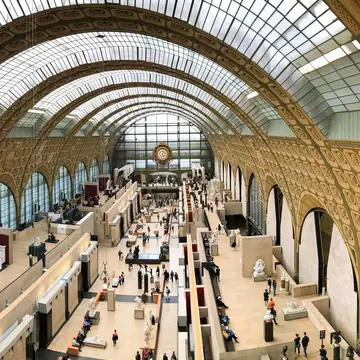 People move around sculptures on display in a vast exhibition space in a former train station with galleries to the side.