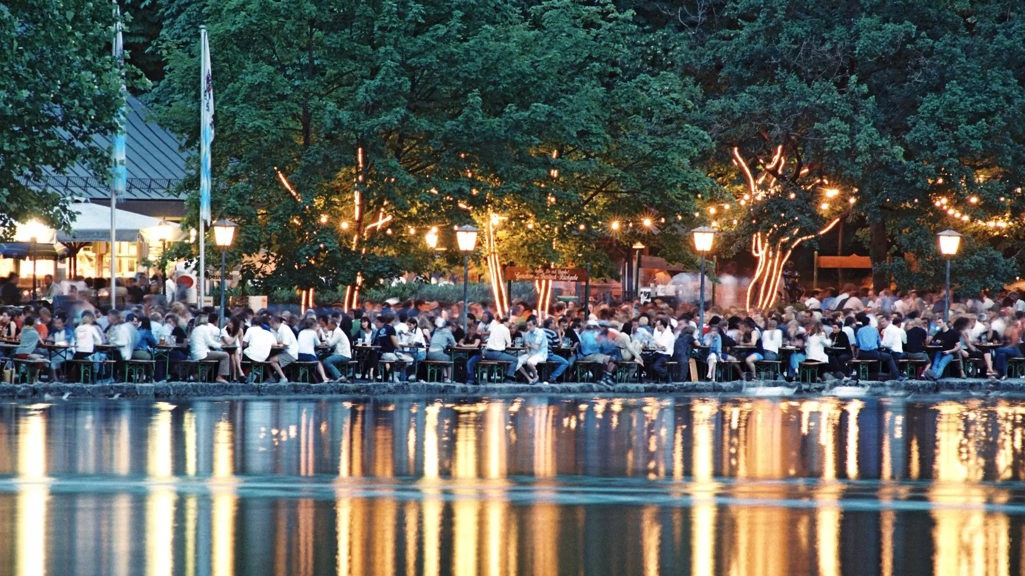 A pool table sits under a crystal chandelier in front of a deep purple wall decorated with a colorful illustration of tropical plants. A white midcentury modern chair sits in the corner and white French doors sit at the far end of the pool table