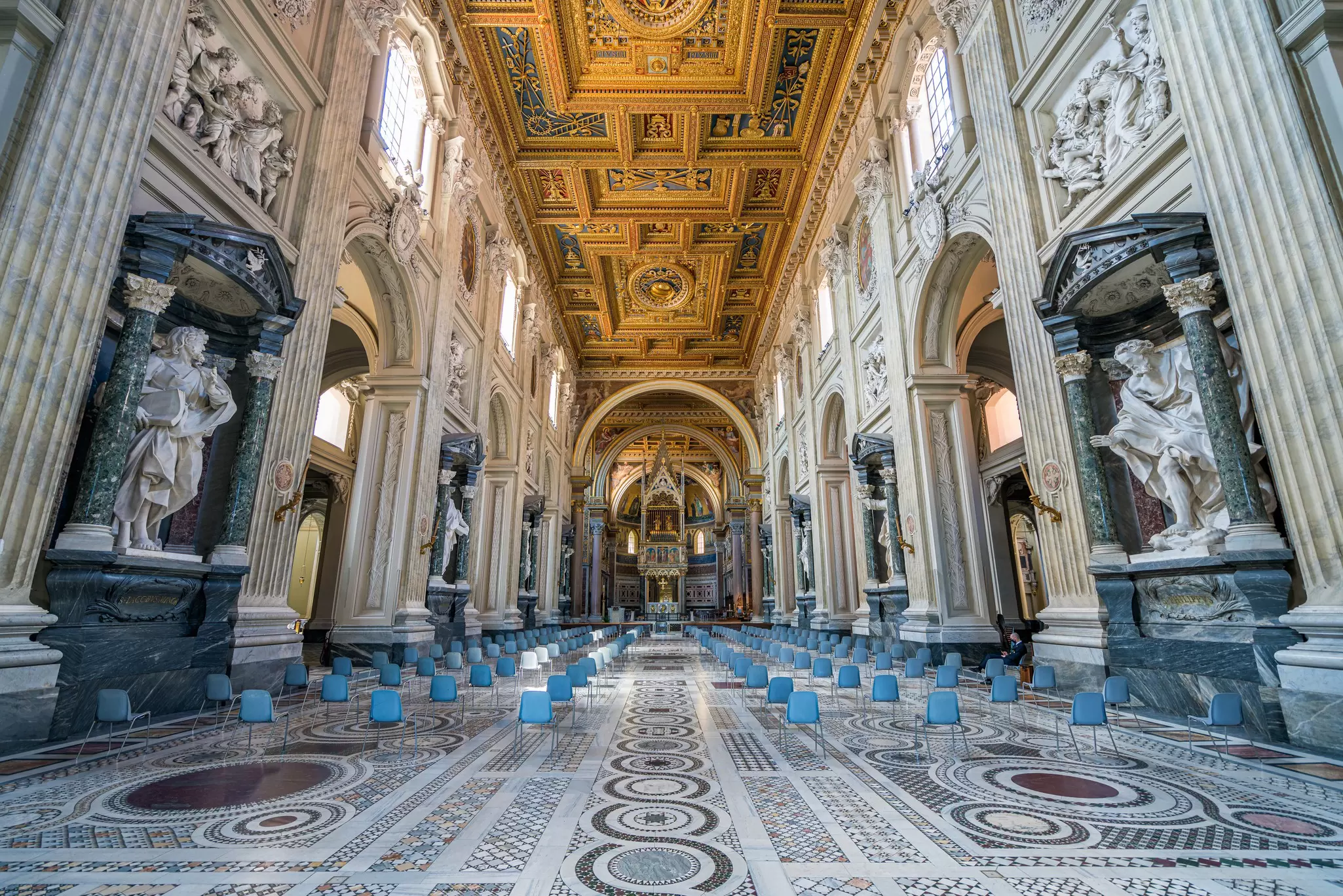 An elaborately decorated church, with patterned marble floors, carved columns and a gold vaulted ceiling.