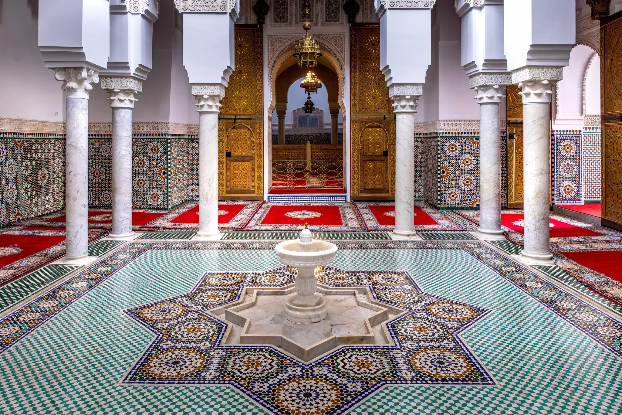 A fountain in the center of a courtyard in Morocco; the floor and walls are covered in spectacular tile patterns.
