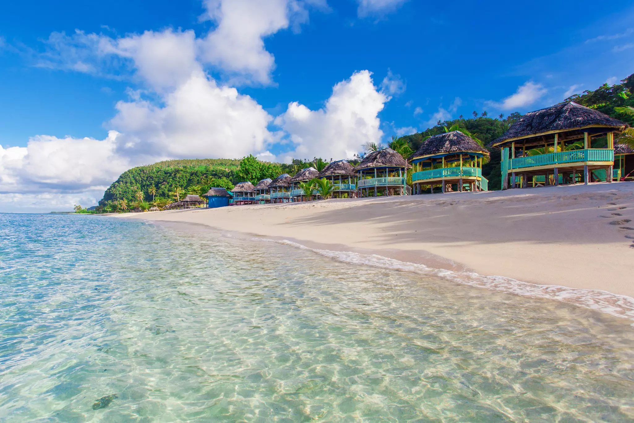 A row of thatched huts on a beach.