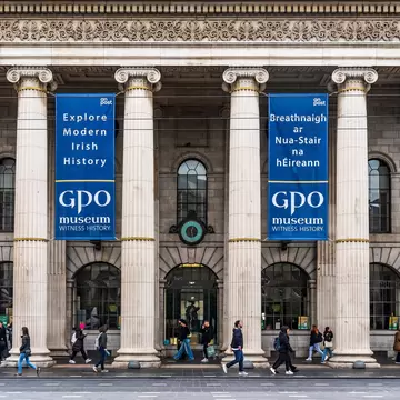 Neoclassical facade of General Post Office, headquarters of leaders of Easter Rising, in O'Connell Street, Dublin city center, Ireland. Pedestrians walking past.