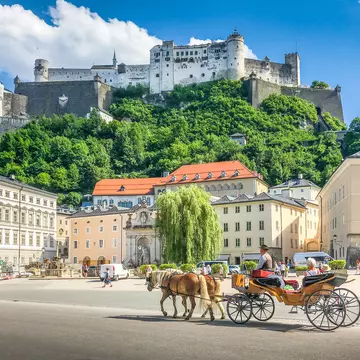 Beautiful panoramic view of the historic city of Salzburg with traditional horse-drawn fiaker carriage and  Hohensalzburg Fortress in summer