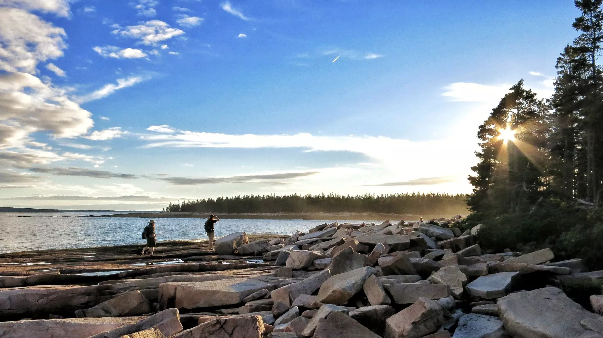 Two people walk along a coastline at low tide looking in the rock pools on the Wonderland Trail, Acadia National Park