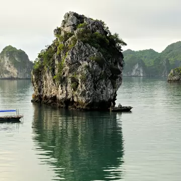 Small boats near rocky karst islets in a sheltered bay in the Halong Bay area, Vietnam.