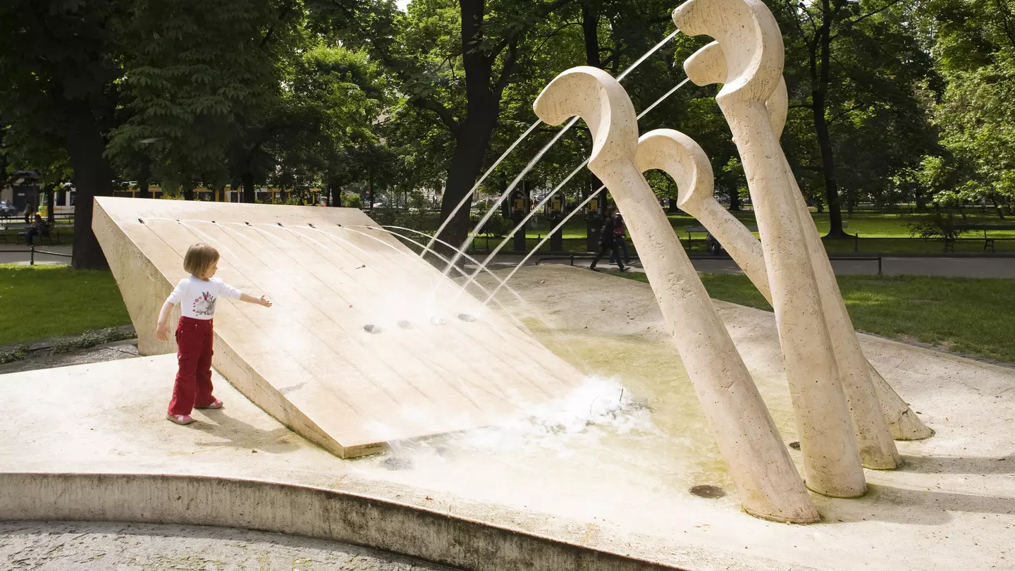 A child plays at a fountain in a park, with jets of water coming from piano keys