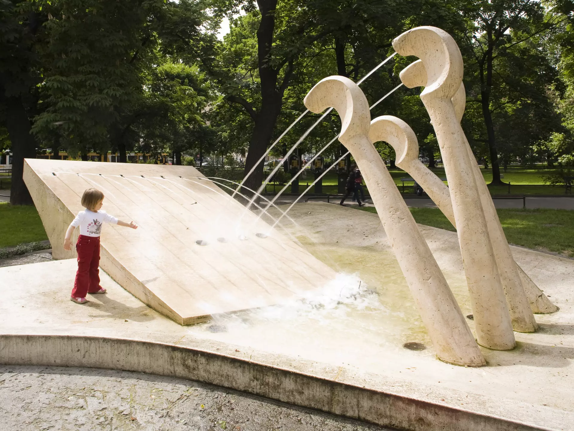 A child plays at a fountain in a park, with jets of water coming from piano keys