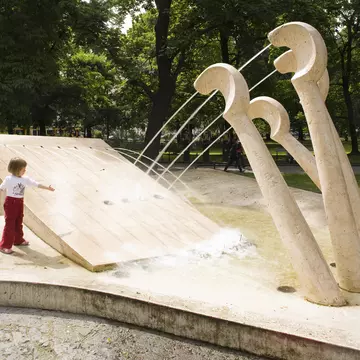 A child plays at a fountain in a park, with jets of water coming from piano keys