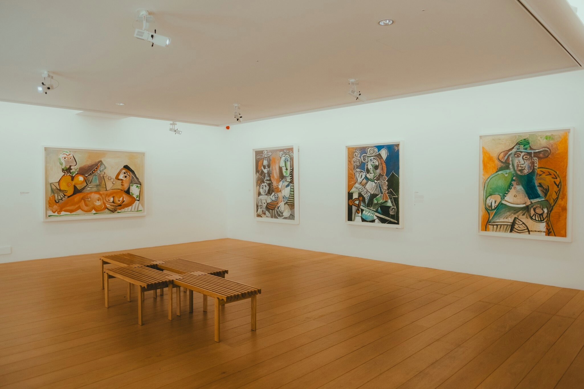 Interior of the Picasso Museum in Paris, featuring colorful abstract paintings on white walls, wooden floors, and minimalist benches.