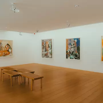Interior of the Picasso Museum in Paris, featuring colorful abstract paintings on white walls, wooden floors, and minimalist benches.