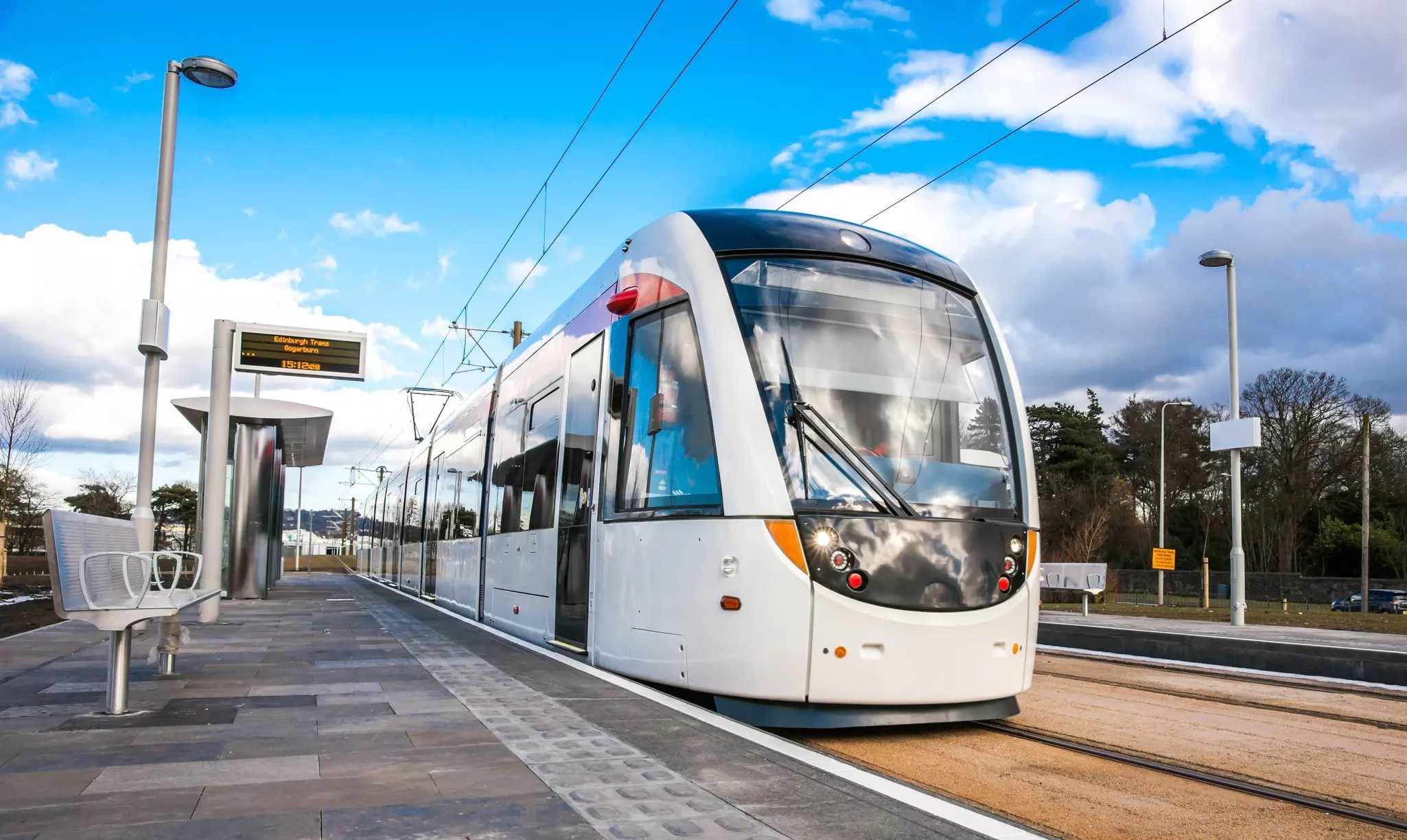 A sleek white tram waits at a platform at a tram stop