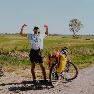 A man flexes his muscles on the side of the road next to two bikes. 