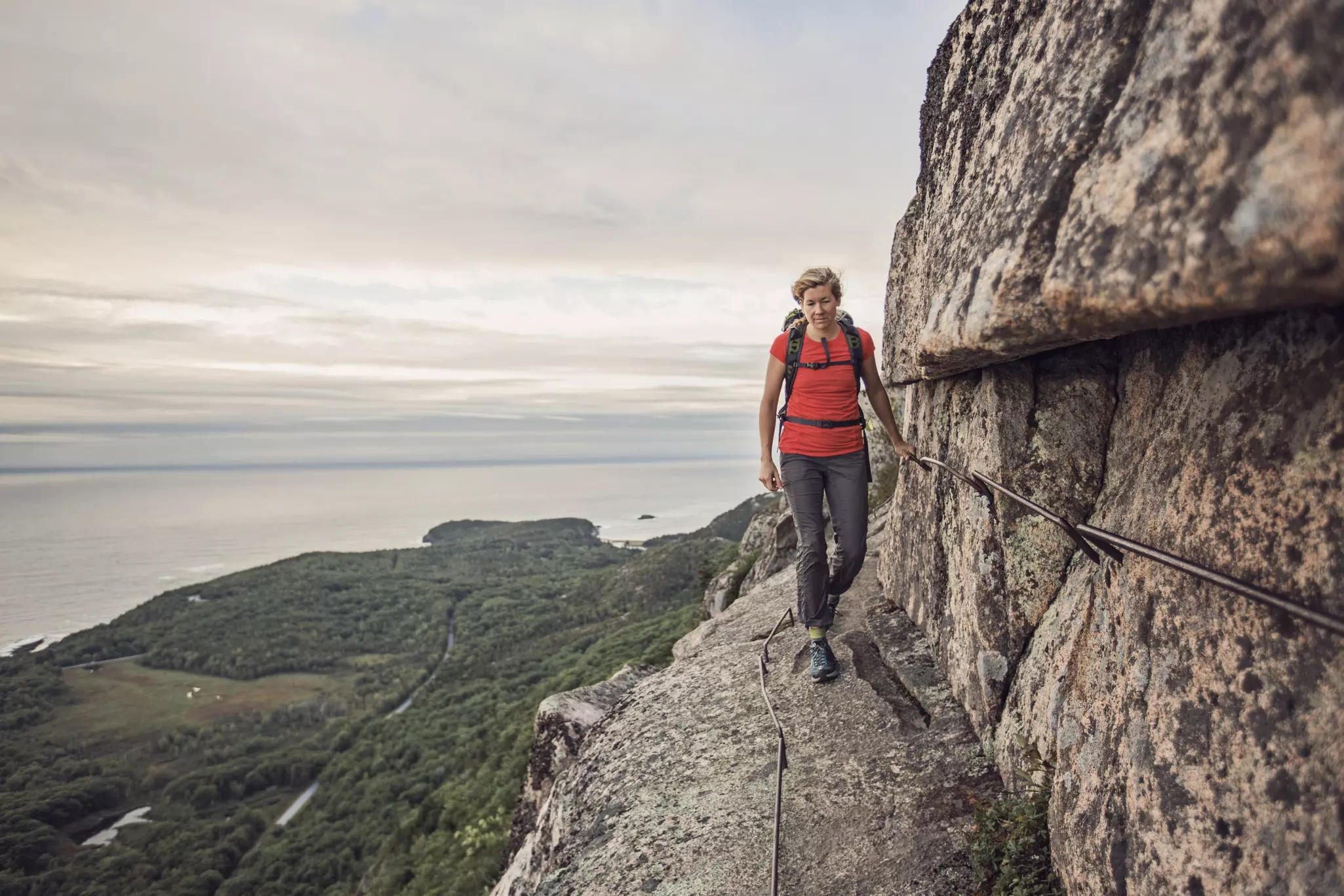 A woman hikes along the cliff edge in Maine's Acadia National Park
