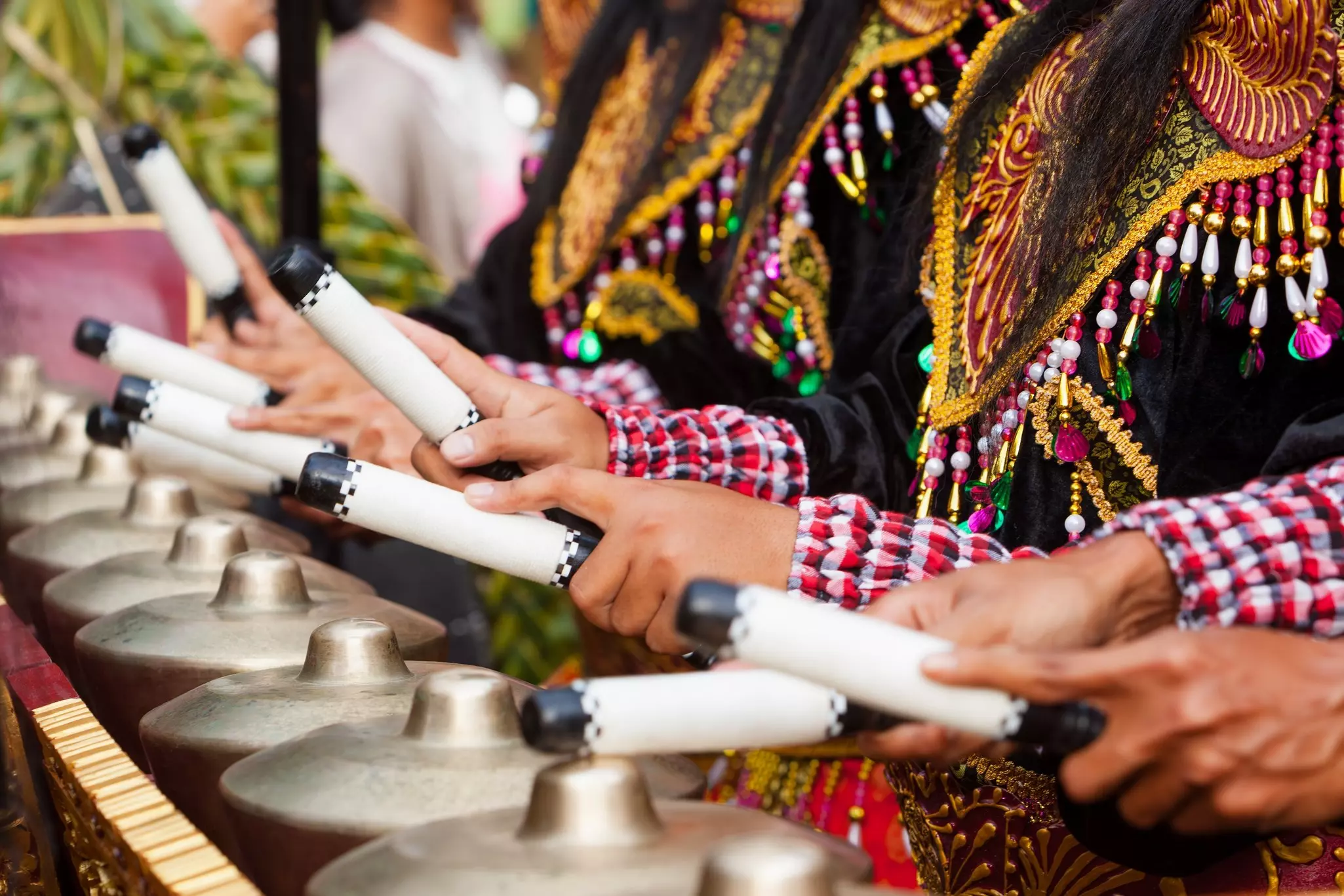 Drummers in black beaded garments play traditional gongs in a line.