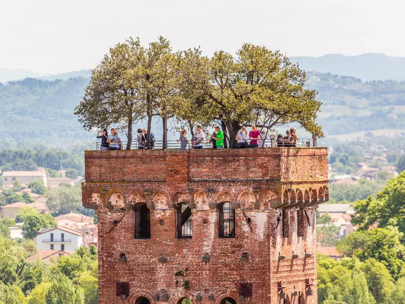 People stand at the top of a red-brick tower with trees on top in Italy. 