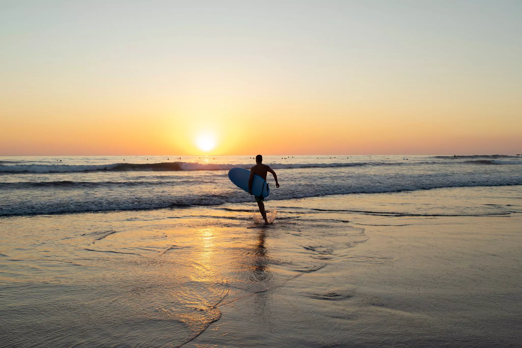 A male running toward the waves with his surfboard under his arm to go surf during the sunset on a beach in Nosara, Costa Rica