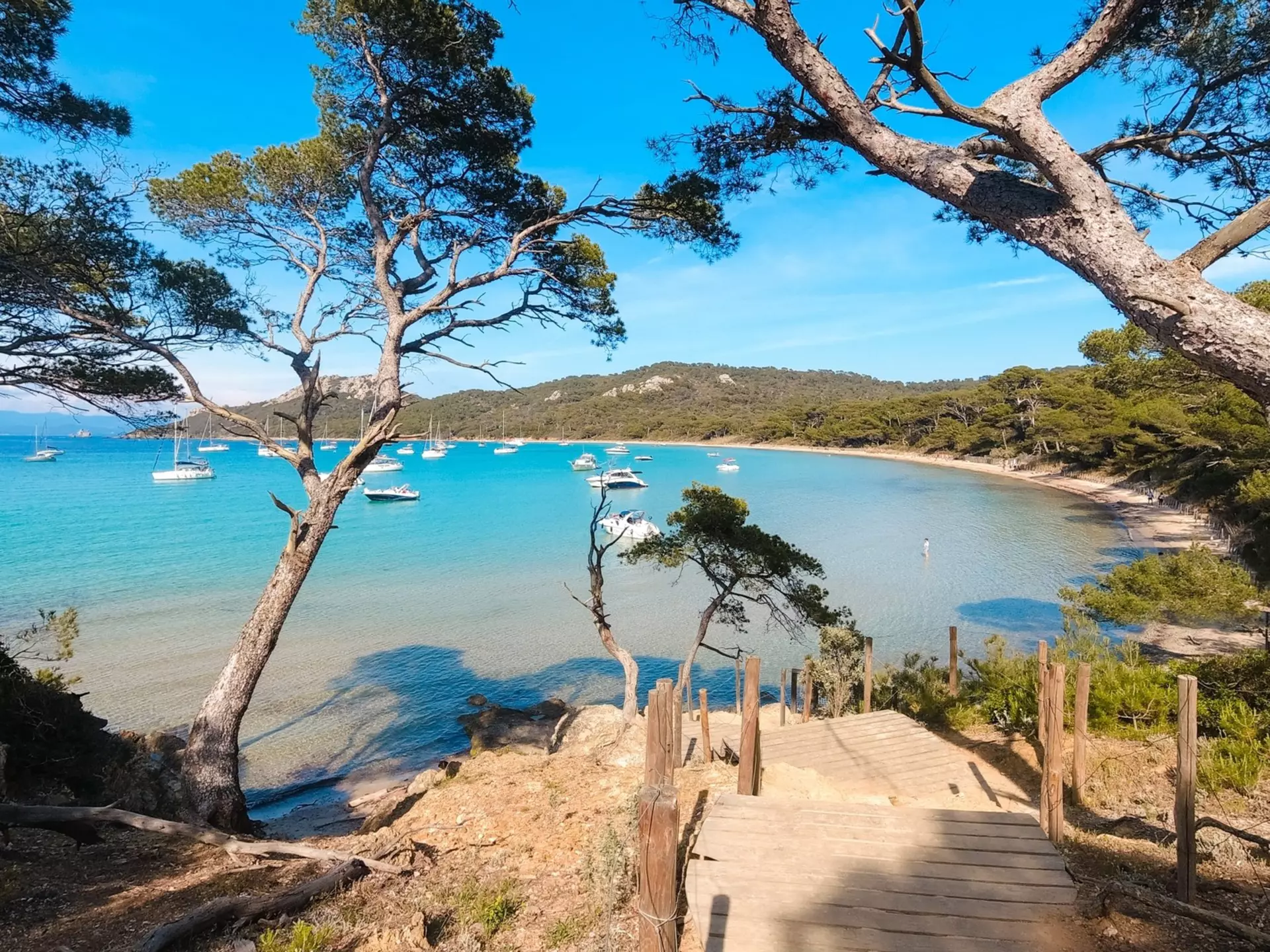 A wood pathway leads to a deep blue cove with boats.
