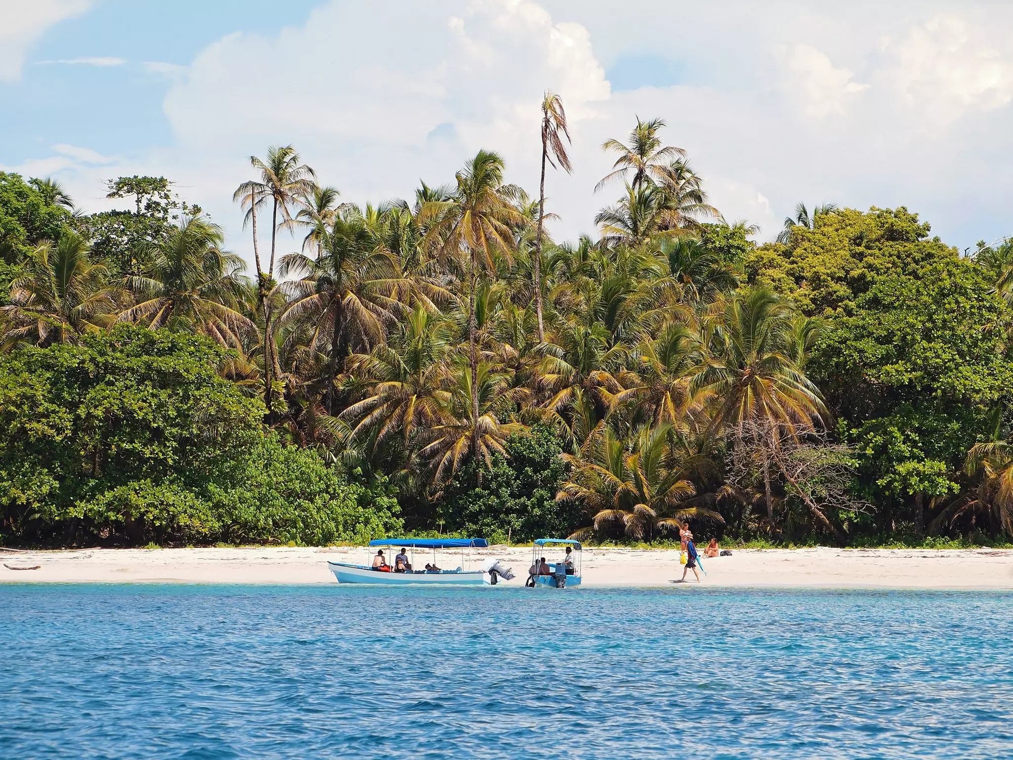 Tourists clamber out of a boat that's moored at the edge of a jungle-lined beach in Parque Nacional Marino Isla Bastimentos, Panama.