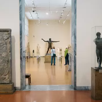 A large bronze statue of a man being admired in a gallery: the National Archaeological Museum in Athens, Greece