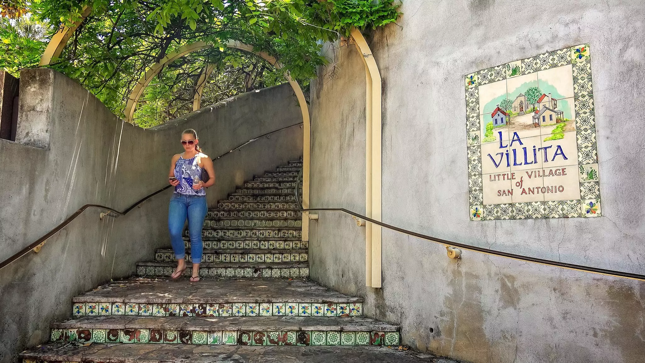 A woman in blue jeans walks down steps with decorative tiles in San Antonio, Texas.