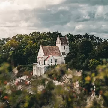 Højerup Gamle Kirke in Stevns, Denmark. Surrounded by trees and cliffs.