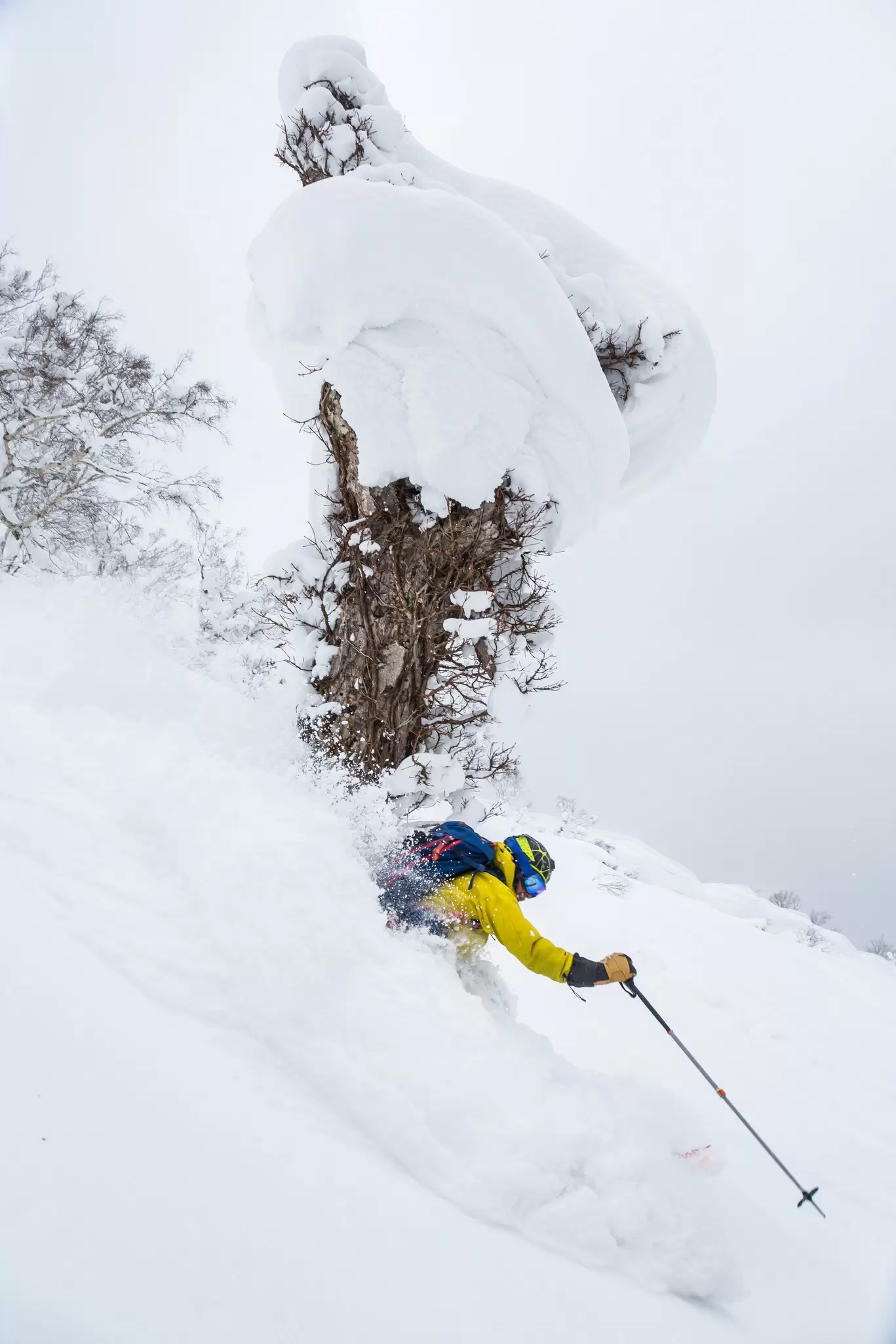 A skier wearing yellow kicks up a spray of snow on a steep downhill slope.