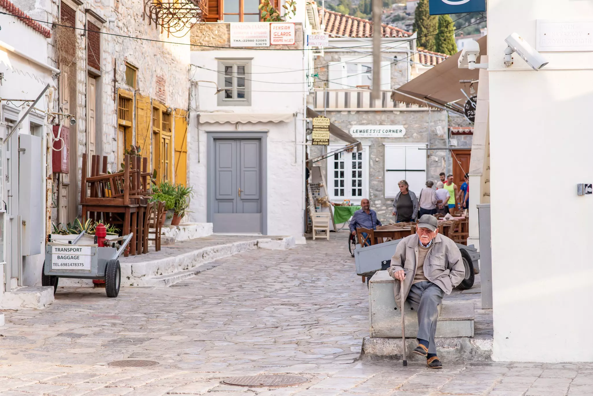 An older gentleman sits and enjoys the day outside a cafe on a cobblestone street