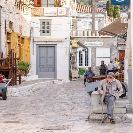 An older gentleman sits and enjoys the day outside a cafe on a cobblestone street