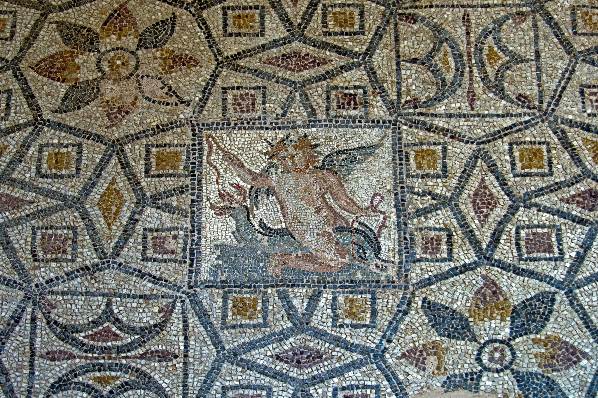 A mosaic floor depicts a winged god and geometric motifs.