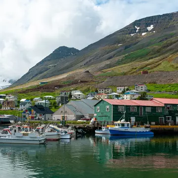 Siglufjörður harbor in North Iceland with fishing boats, colorful houses and church surrounded by mountains. Scenic coastal town with calm water and traditional village atmosphere in Icelandic landscape.