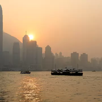 The ferry crossing Victoria Harbour at sunset, Hong Kong, with the city skyline silhouetted behind. 