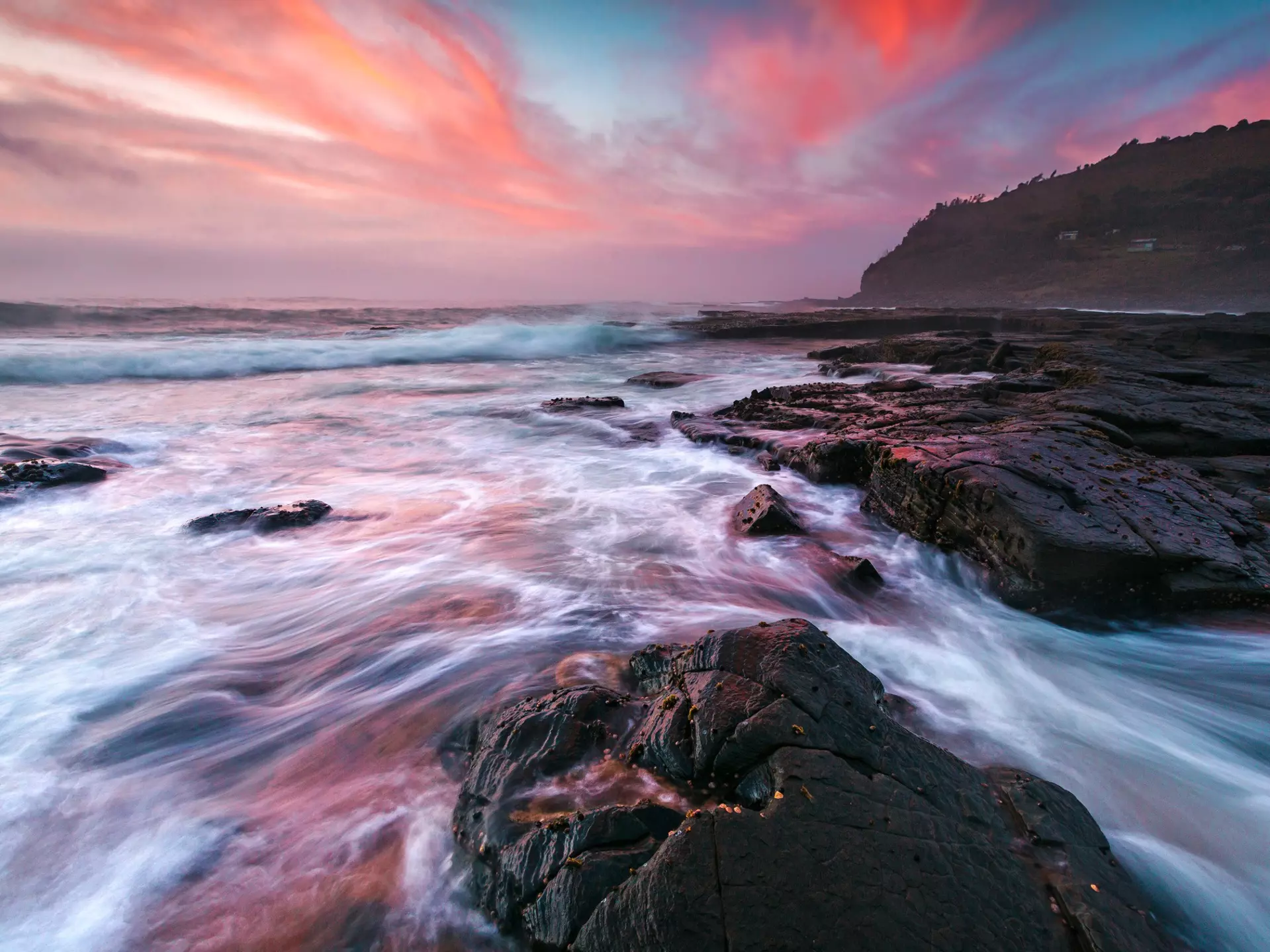 Waves wash onto coastal rocks with colourful clouds in the sky, Garie Beach.