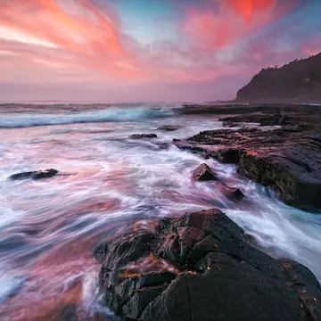 Waves wash onto coastal rocks with colourful clouds in the sky, Garie Beach.
