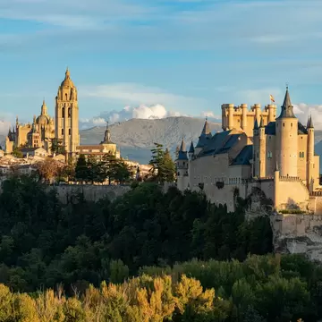 Segovia's turreted Alcázar stands on a rocky crag above woodland, with the cathedral tower and old town behind