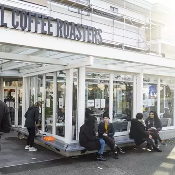 People wait in line outside a coffee shop in the West 4th shopping district in Vancouver, British Columbia, Canada.