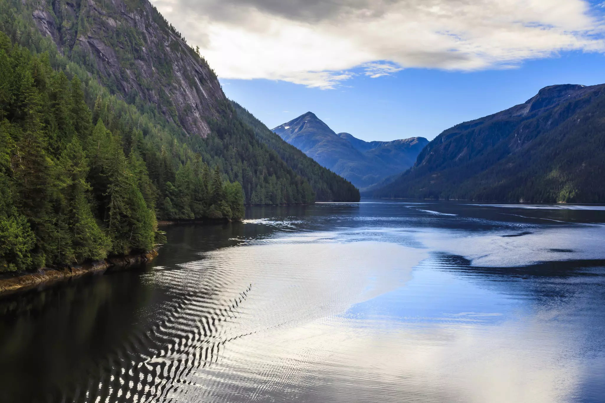 Rippling waters surrounded by greenery and mountains under a blue sky