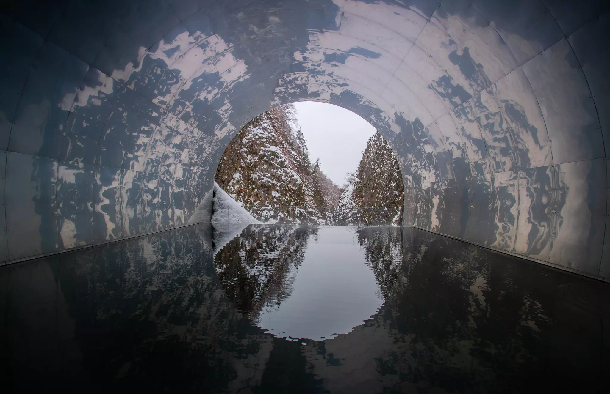 A snowy landscape in Japan is visible through a tunnel with an art installation.