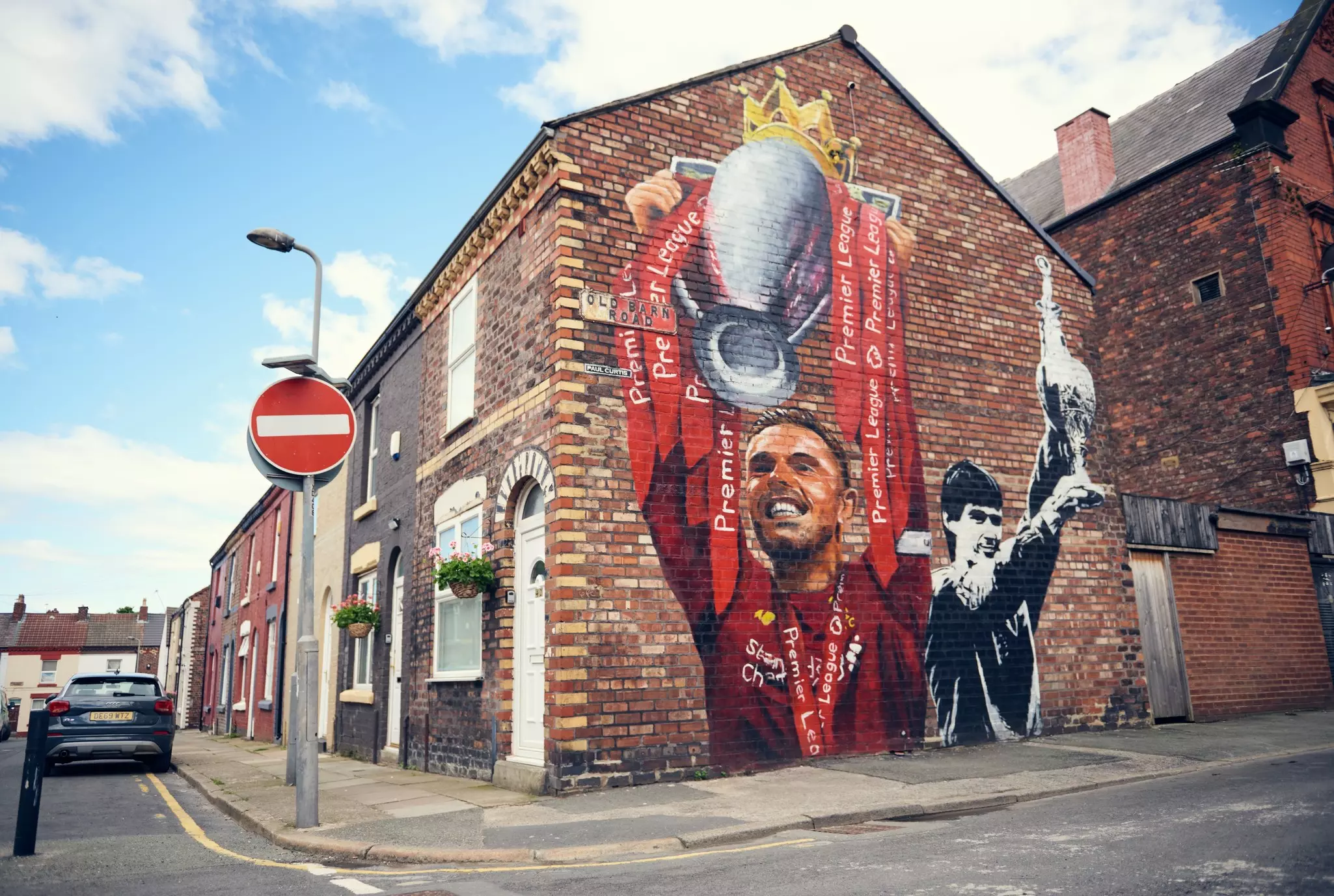 A painting of a football player dressed in red holding aloft a trophy on the side of a house in a residential area.