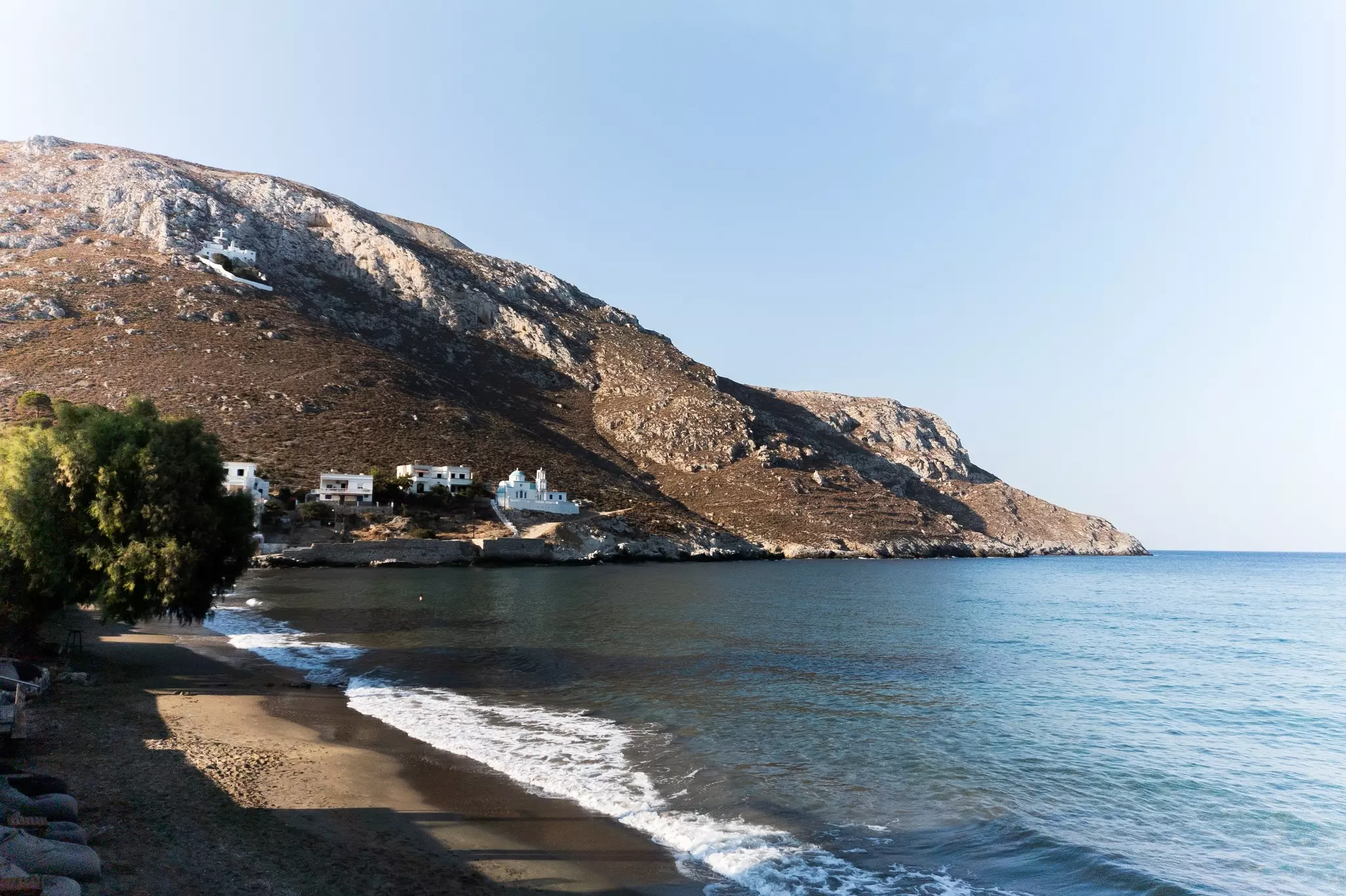 Small white buildings built into a hillside close to the water; a beach curves around the water toward the buildings.