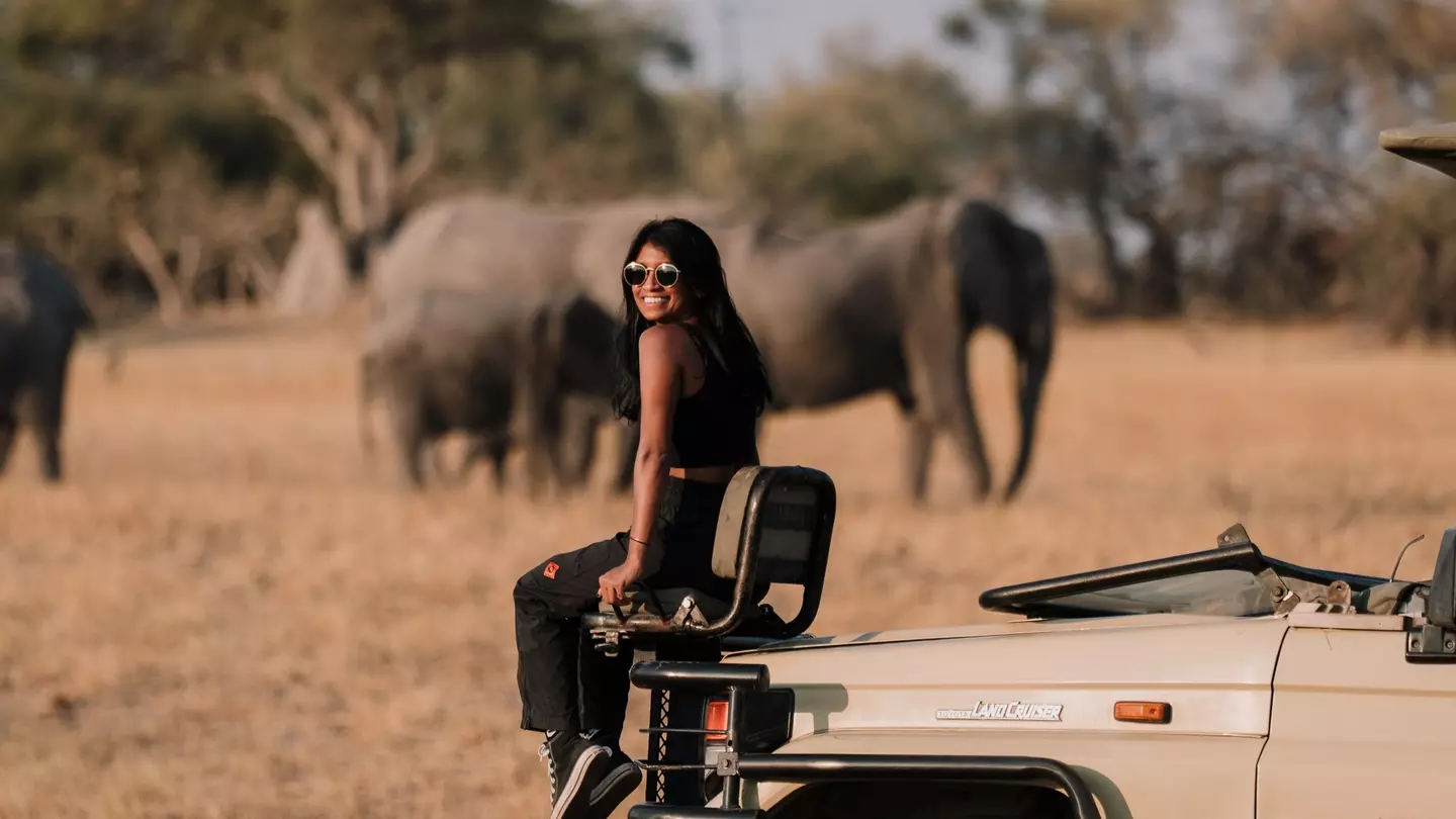 Lonely Planet staff member Deepa Lakshmin sitting on a safari jeep with elephants in Botswana.