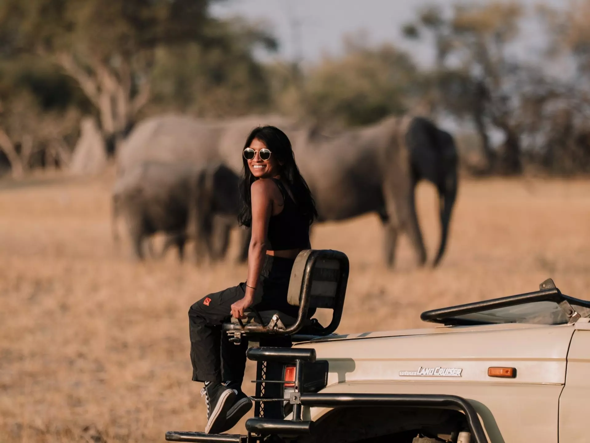 Lonely Planet staff member Deepa Lakshmin sitting on a safari jeep with elephants in Botswana.