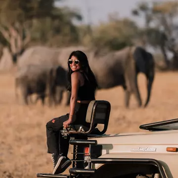 Lonely Planet staff member Deepa Lakshmin sitting on a safari jeep with elephants in Botswana.