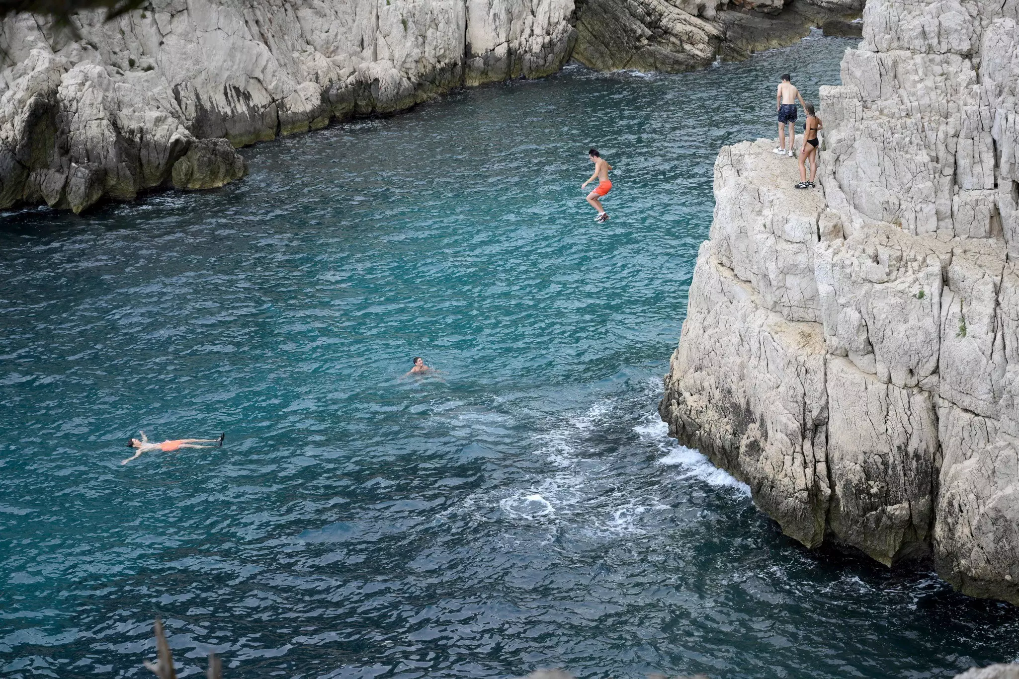 Young people jump from cliffs into blue sea